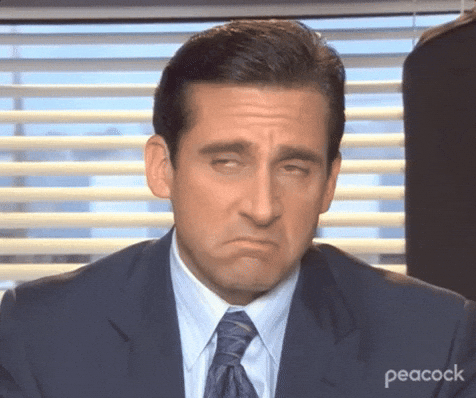 Michael Scott z The Office siedzi przy biurku i patrzy z niedowierzaniem w kamerę, unosząc brwi – popularny gif z serialu, idealny do wyrażenia zaskoczenia lub ironii.